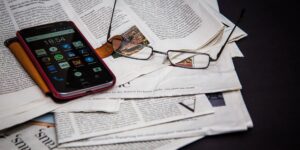 Photo of a newspaper, phone and reading glasses
