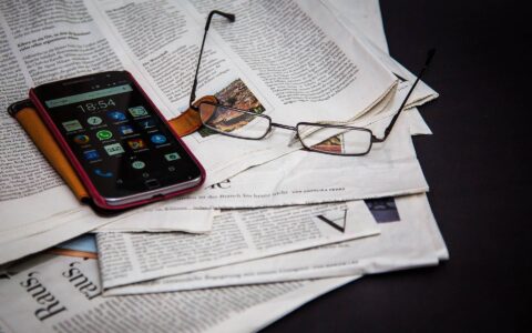Photo of a newspaper, phone and reading glasses